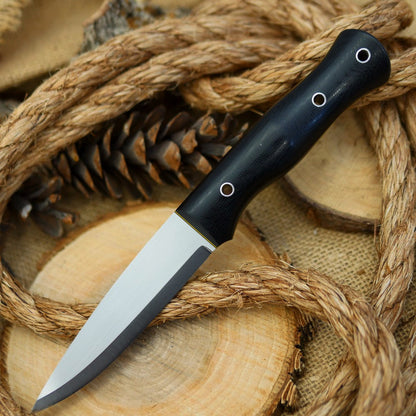 An Adventure Sworn bushcraft knife with black canvas micarta handle scales and black and yellow liners.